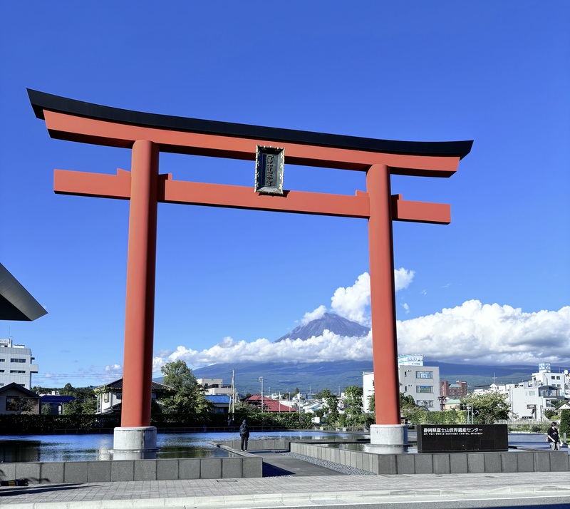 晴れた青空の下、大きな朱色の鳥居の向こうに雪をかぶった富士山が見える風景。